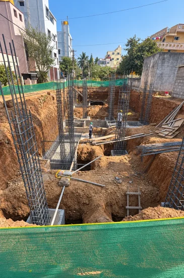 Residential foundation construction in Bengaluru at the Sanjay Singh project, showing excavated footing pits and column reinforcement during the early construction stage.