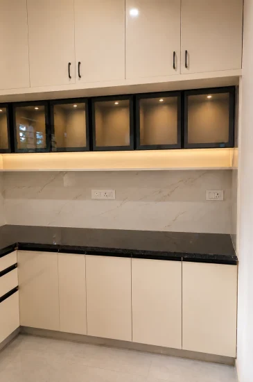 Completed L-shaped kitchen design in Bengaluru for the Sanjay Singh project, with light-coloured cabinets, a dark countertop and illuminated glass-front cabinets.