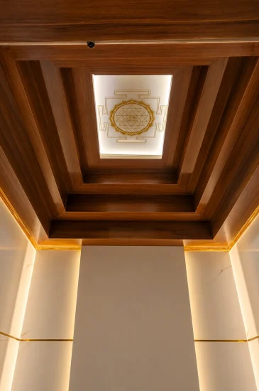 Completed pooja room ceiling design at the Laxman project in Bengaluru, with layered wood finish panels and warm recessed lighting.