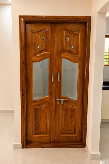 Completed wooden double door design in Bengaluru for the Laxman project, with carved panels, glass inserts and a matching wood frame.