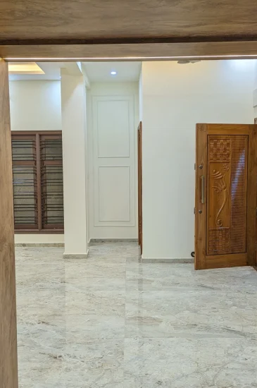 Entrance hall interior at the completed Palaksha Residency in Bagalgunte, Bangalore, showing wood-finish door frames, a tiled floor and the living area beyond