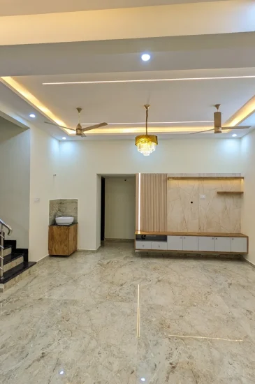 Living room interior at the completed Palaksha Residency in Bagalgunte, Bangalore, showing a recessed false ceiling with lighting and a staircase to the left