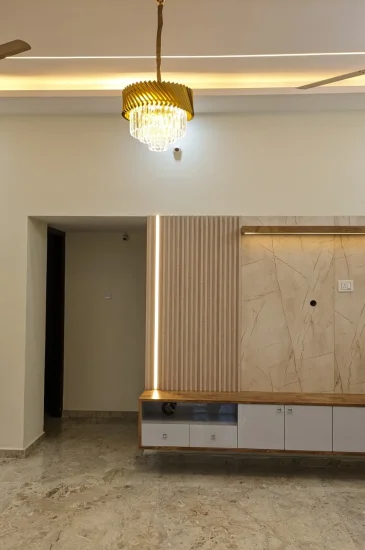 Living room TV wall design at the completed Palaksha Residency in Bagalgunte, Bangalore, with a wood-finish panel, floating console and recessed ceiling lighting